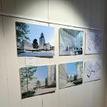 Une exposition de photographies d'architecture et de plans d'étage est montée sur un mur blanc. Les images présentent des conceptions de bâtiments modernes et des espaces intérieurs avec des personnes.